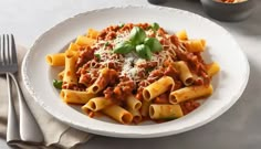 pasta with meat sauce and parmesan cheese on white plate next to silverware