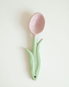 a pink and green vase sitting on top of a white wall next to a spoon