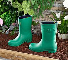 a pair of green rain boots sitting on top of mulch next to some flowers