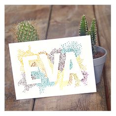 a card with the word eva written in multicolored letters next to a cactus