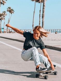 a woman riding a skateboard down the side of a road next to palm trees