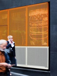 people walking down the street in front of a building with an advertisement on it's side