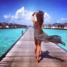 a woman is walking on a dock over the water with her hair blowing in the wind