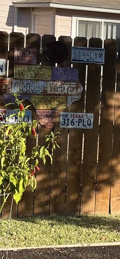 a wooden fence with several signs on it and a tree in front of the house