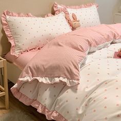 a bed with pink and white polka dot comforter, pillows and stuffed animals on it