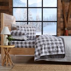 a bed with plaid sheets and pillows in front of a window overlooking the snow covered mountains