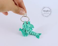 a hand holding a keychain with a small green toy in the shape of a seahorse