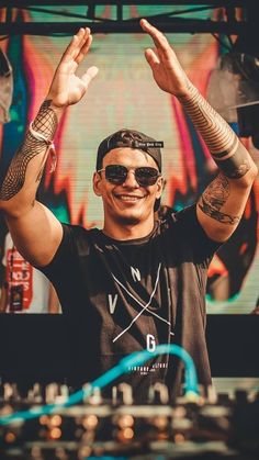 a man with tattoos and sunglasses standing in front of a dj booth holding his hands up