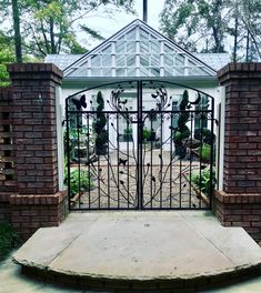 an iron gate in front of a brick building with a white roof and trees behind it