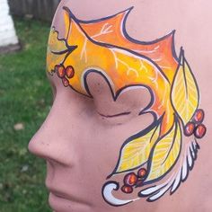 a face painted with leaves and berries on the side of a mannequin's head