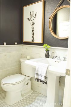 a white toilet sitting next to a bathroom sink under a framed giraffe painting