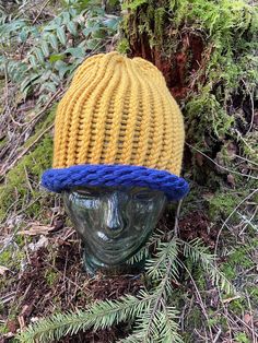 a yellow and blue knitted hat sitting on top of a head in the woods