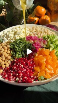 a white bowl filled with different types of vegetables and fruits next to oranges on a table