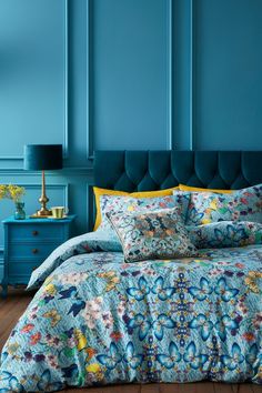 a bedroom with blue walls and a bed covered in floral comforter covers, pillows and throw pillows