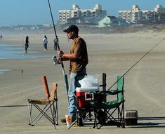 a man standing on top of a beach next to a chair holding a fishing pole