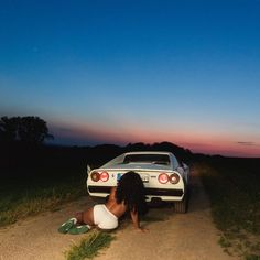 a woman laying on the side of a road next to a white car at night