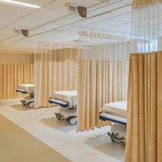 an empty hospital room with beds and medical equipment on the floor in front of sheer curtains