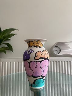 a colorful vase sitting on top of a glass table next to a potted plant