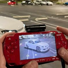 a person holding up a red camera to take a picture of a car on the street