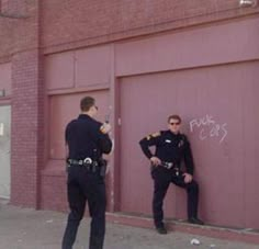 two police officers standing in front of a garage door with graffiti on the wall behind them