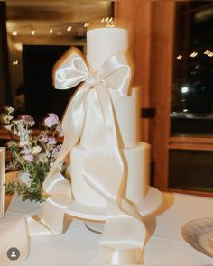 a white wedding cake with a large bow on top and flowers in the bottom tier