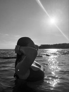 a woman sitting in the water with her hands on her head and looking at the sun