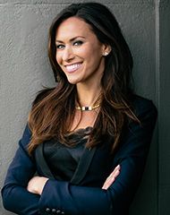 a woman standing with her arms crossed in front of a gray wall and smiling at the camera