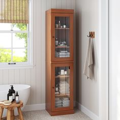 a wooden cabinet with glass doors in a bathroom next to a bathtub and window