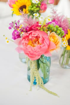 three vases filled with colorful flowers sitting on a white table cloth covered tablecloth