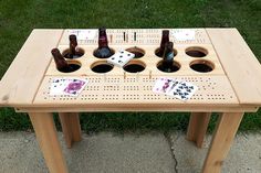 a wooden table with beer bottles and dominos on it in front of some grass