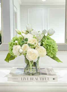 a vase filled with white and green flowers on top of a table next to a mirror