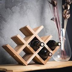 a wooden wine rack with bottles in it on a table next to a vase and dried flowers