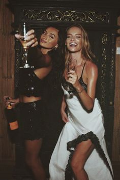 two beautiful young women standing next to each other holding wine glasses in their hands and posing for the camera