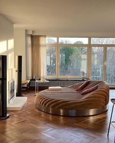 a living room with a large round couch and wooden floors in front of two windows