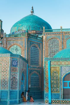 two women sitting on the ground in front of a building with blue and green tiles