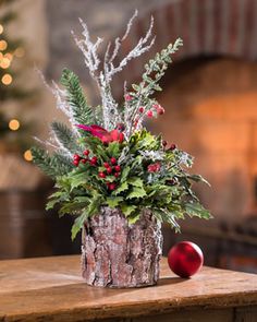 a wooden table topped with a vase filled with flowers and greenery next to a fire place