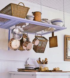 pots and pans hanging from the ceiling in a kitchen with white walls, wooden flooring and blue shelves