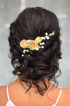 the back of a woman's head, with flowers in her hair and an orange rose pinned to it