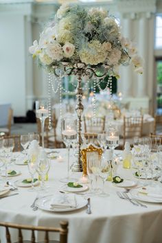 an elegant centerpiece with white flowers and greenery sits atop a table set for a formal dinner