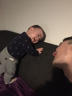 a man holding a baby up to his face while laying on top of a couch