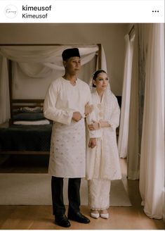 a man and woman standing next to each other in front of a bed with curtains