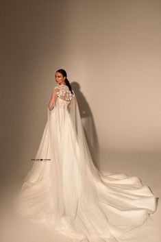 a woman in a white wedding dress standing with her back to the camera, wearing a long veil