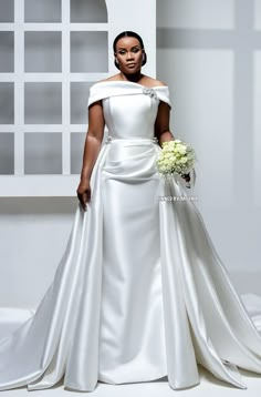 a woman in a white wedding dress holding a bouquet and posing for the camera with her hands on her hips