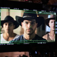 two men wearing hats are on the screen in front of a camera set up for filming