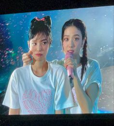 two young women standing next to each other in front of a tv screen holding microphones