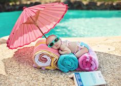 a baby doll laying on top of a towel next to a pool with an umbrella