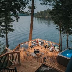 a deck with chairs and lights next to a body of water in the evening time