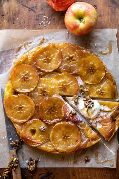 an apple tart with slices missing from it on a piece of parchment paper next to two apples