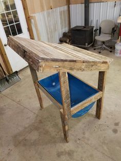 a wooden table sitting inside of a garage next to a blue bucket on the floor