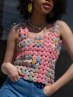 a woman wearing a crochet top and denim shorts stands in front of a window